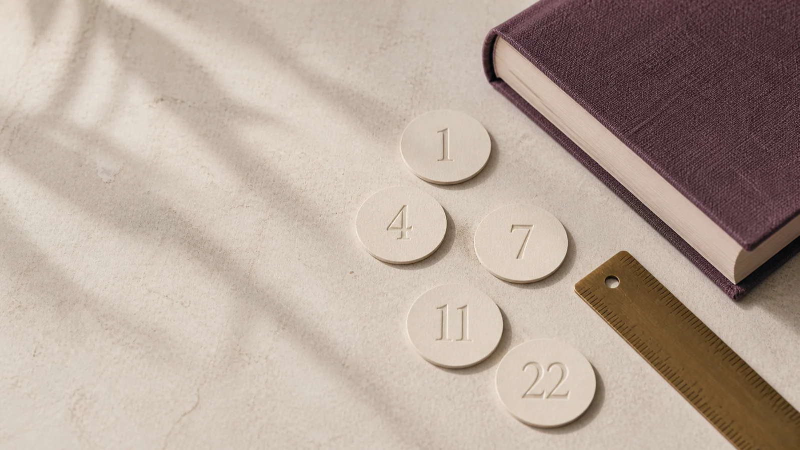 Ivory number discs beside an aubergine journal and brass ruler